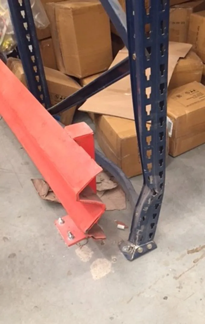 Red steel barrier snapped off next to a damaged pallet rack upright