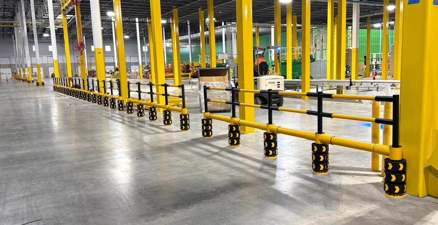 A long run of ENNAT double guardrail protecting a warehouse aisle, with a forklift operating right beside it